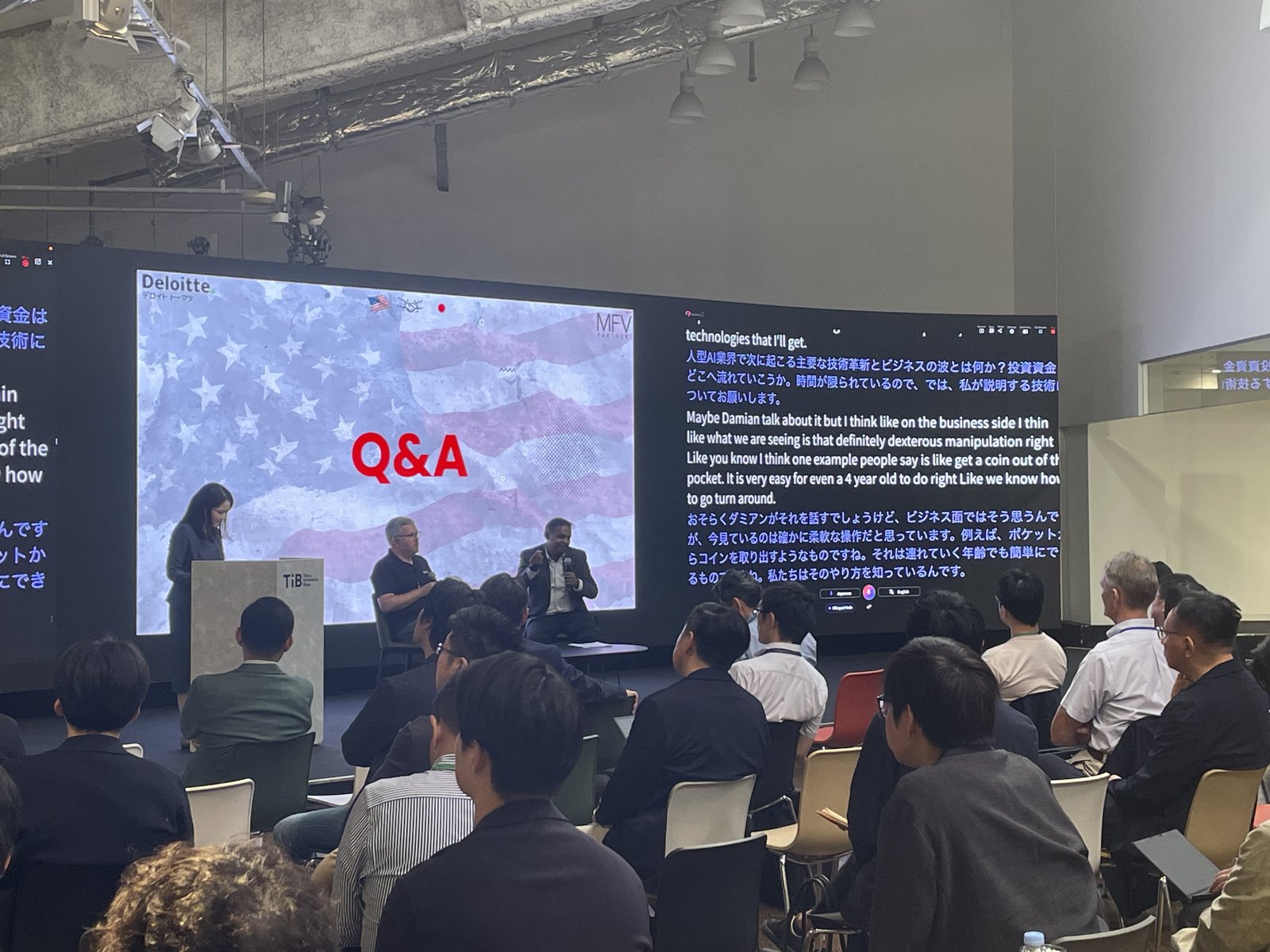 The live Q&A underway: speakers seated on stage beneath a Q&A slide, with VoicePing’s real-time Japanese-English translation panel running on the screen beside them.