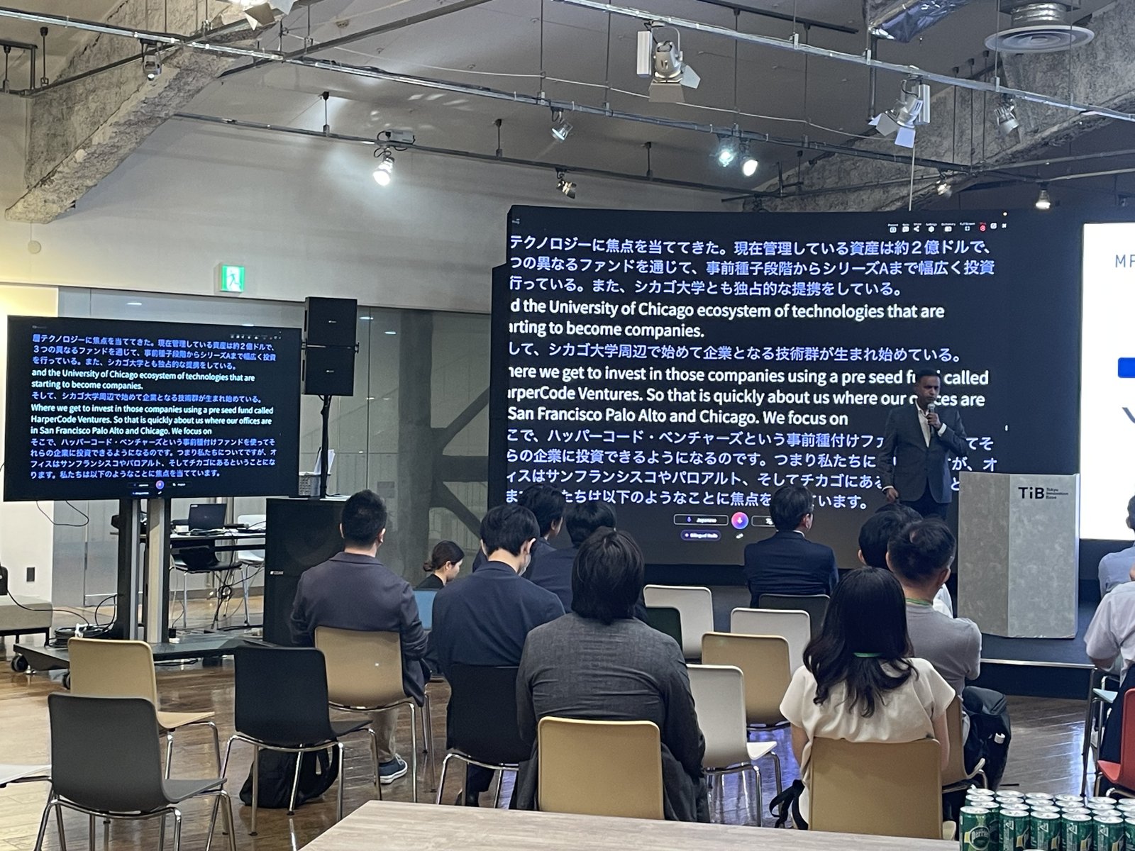 Attendees at Tokyo Innovation Base following the forum, the presenter’s slide and VoicePing’s live translation both visible on the room’s screens.