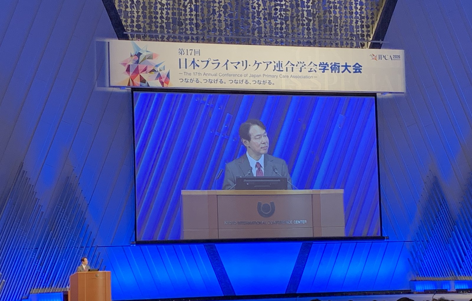 A speaker on the main stage screen at JPCA 2026 in Kyoto.