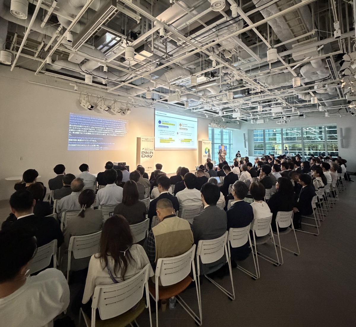 A full room follows the pitches at MedTech ROUND Pitch Day, with the live translation on the screen at the front.