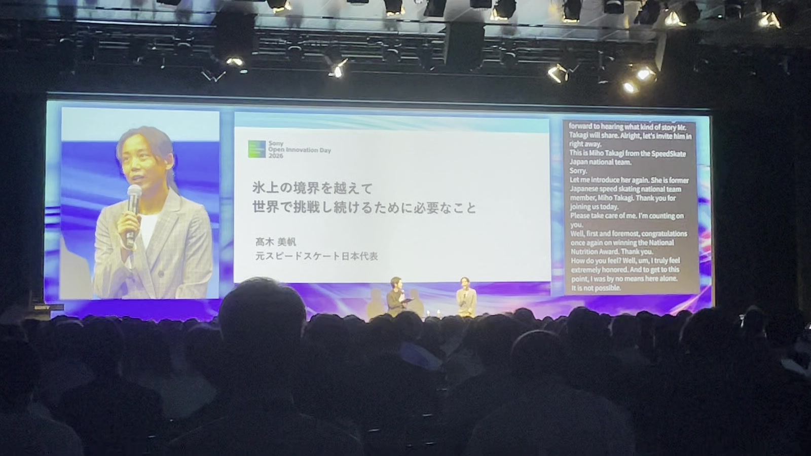 Miho Takagi speaking at Sony Open Innovation Day 2026, with live English subtitles shown on the right side of the main stage screen.