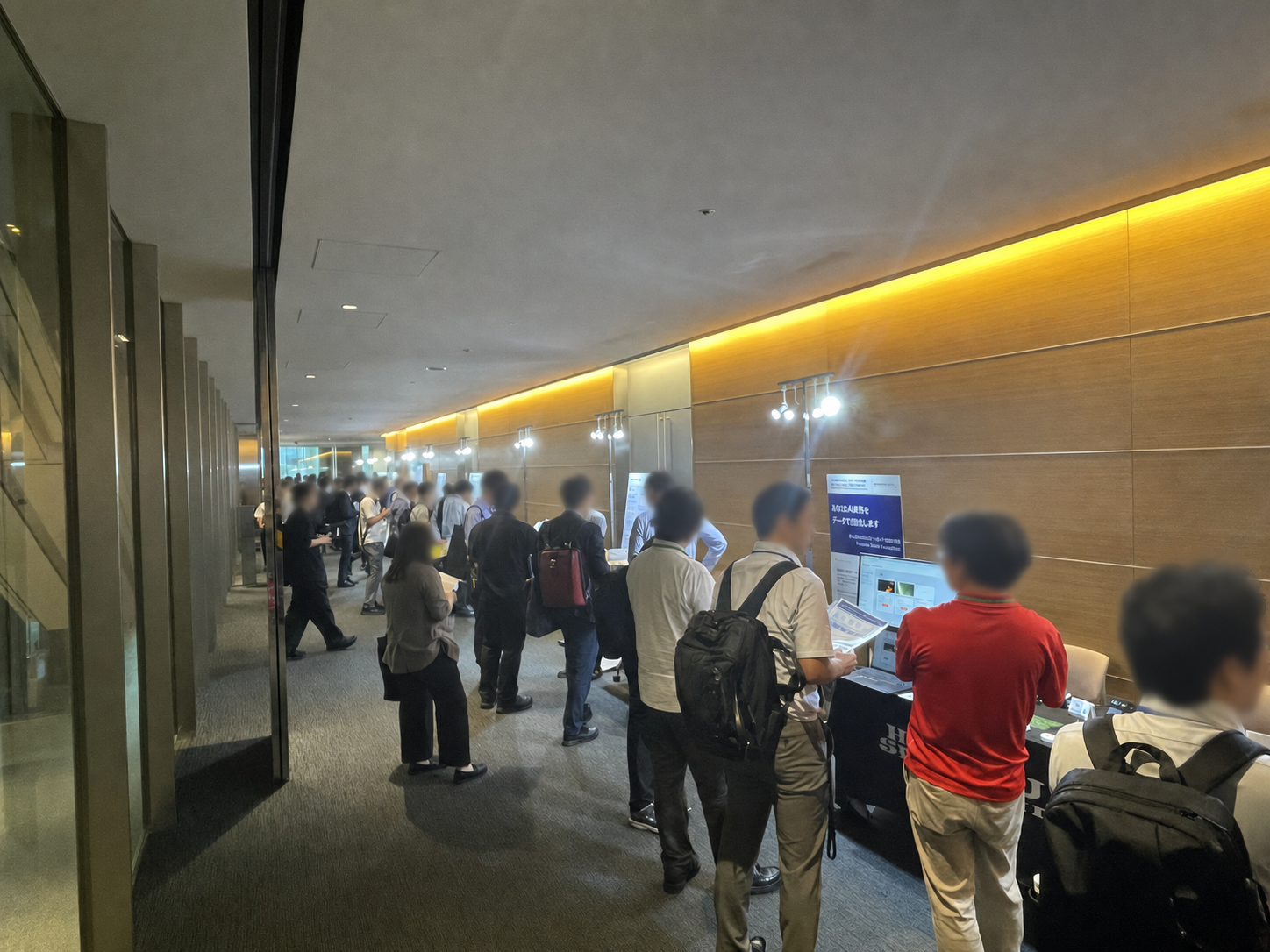 Attendees speaking with exhibitors along the Sony Open Innovation Day 2026 exhibition corridor. Every identifiable non-stage face has been blurred.